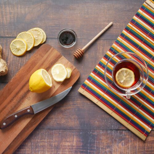 Flat lay of ginger tea with lemon slices, a wooden chopping board, and a honey dipper on a rustic table.