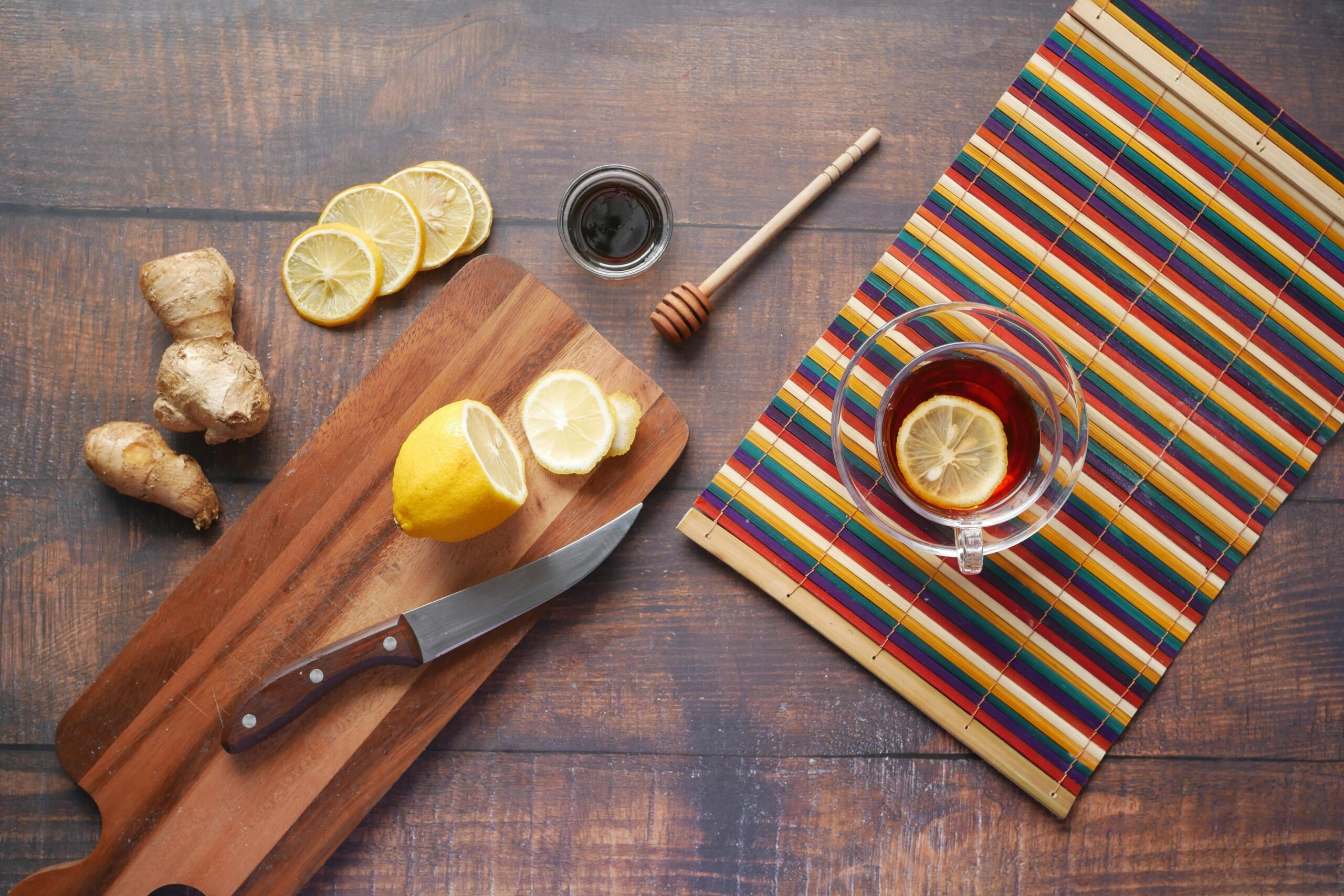 Flat lay of ginger tea with lemon slices, a wooden chopping board, and a honey dipper on a rustic table.